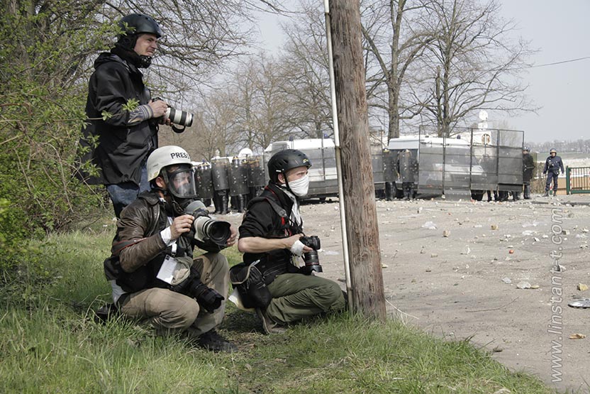 Photographes de presse avec casque et masque à gaz, un barage de police en fond